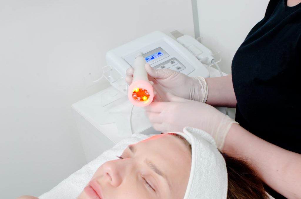 beautician doing led light therapy to female customer in beauty salon. Anti-aging treatments and photo rejuvenation procedure